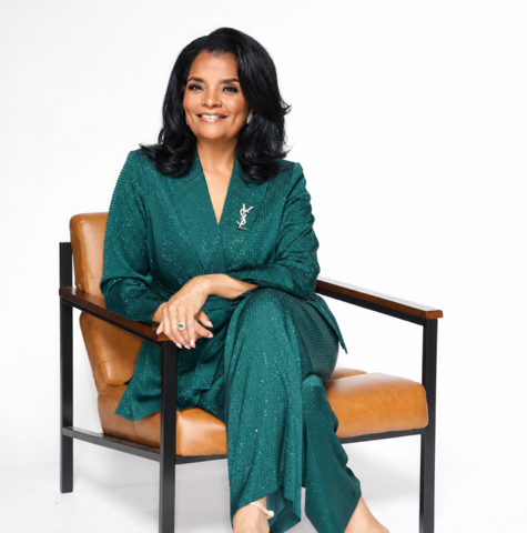 Cynthia Thompson seated in an emerald suit on a tan leather chair